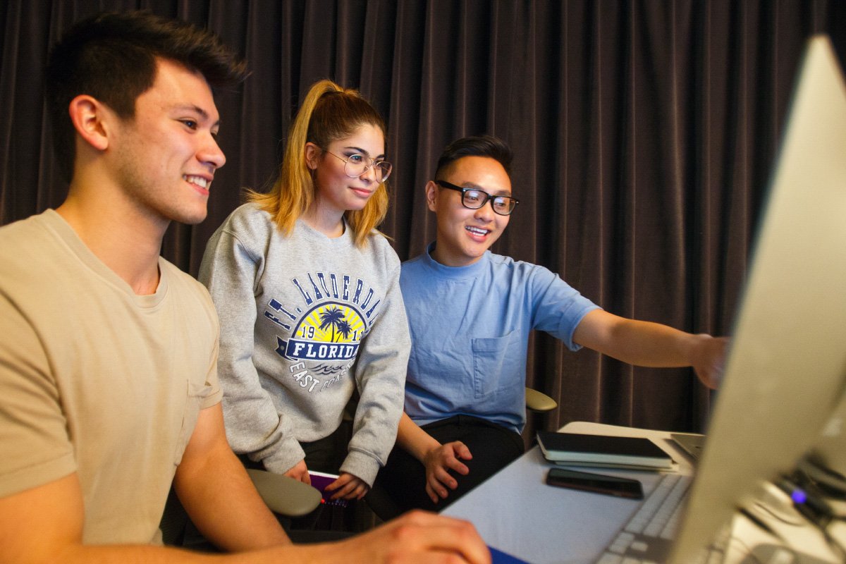 Three students sit in front of a computer